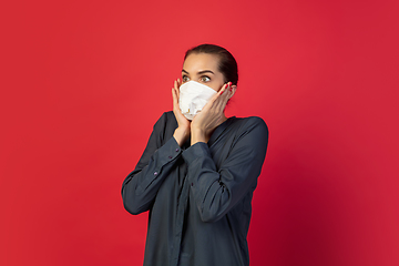 Image showing Woman in protective face mask isolated on red studio background. New rules of COVID spreading prevention