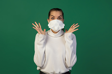 Image showing Woman in protective face mask isolated on green studio background. New rules of COVID spreading prevention