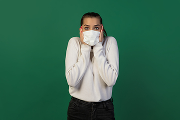 Image showing Woman in protective face mask isolated on green studio background. New rules of COVID spreading prevention