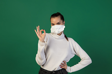 Image showing Woman in protective face mask isolated on green studio background. New rules of COVID spreading prevention