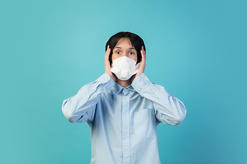 Image showing Man in protective face mask isolated on blue studio background. New rules of COVID spreading prevention