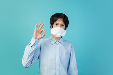 Image showing Man in protective face mask isolated on blue studio background. New rules of COVID spreading prevention