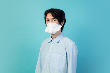 Image showing Man in protective face mask isolated on blue studio background. New rules of COVID spreading prevention