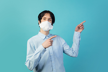 Image showing Man in protective face mask isolated on blue studio background. New rules of COVID spreading prevention