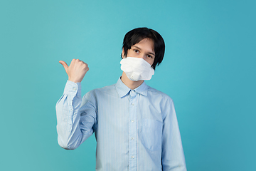 Image showing Man in protective face mask isolated on blue studio background. New rules of COVID spreading prevention