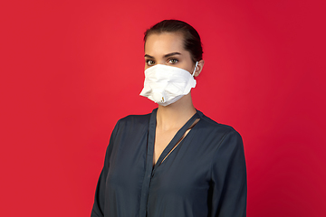 Image showing Woman in protective face mask isolated on red studio background. New rules of COVID spreading prevention
