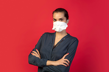 Image showing Woman in protective face mask isolated on red studio background. New rules of COVID spreading prevention