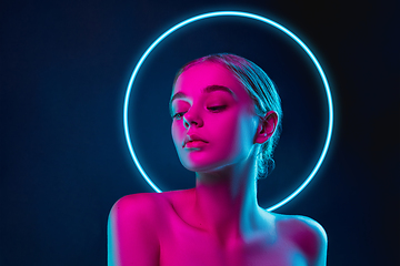 Image showing Portrait of female fashion model in neon light on dark studio background. Beautiful caucasian woman with trendy make-up, neoned blue circle