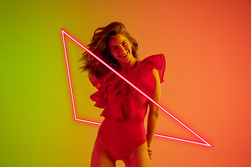 Image showing Beautiful seductive girl in fashionable, romantic outfit on gradient background in neon light with glowing neoned pink triangle