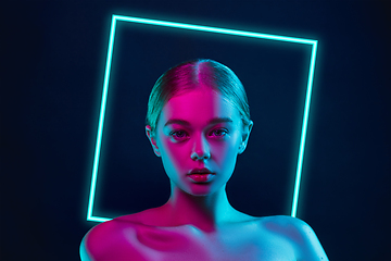 Image showing Portrait of female fashion model in neon light on dark studio background. Beautiful caucasian woman with trendy make-up, neoned blue square