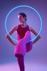Image showing Young and graceful ballet dancer isolated on purple studio background in neon light with glowing neoned circle. Art, motion, action, flexibility, inspiration concept.