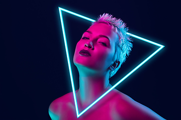 Image showing Portrait of female fashion model in neon light on dark studio background. Beautiful caucasian woman with trendy make-up, neoned blue triangle