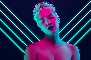 Image showing Portrait of female fashion model in neon light on dark studio background. Beautiful caucasian woman with trendy make-up, neoned blue lines