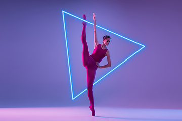 Image showing Young and graceful ballet dancer isolated on purple studio background in neon light with glowing neoned triangle. Art, motion, action, flexibility, inspiration concept.