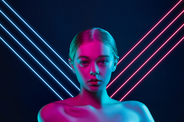 Image showing Portrait of female fashion model in neon light on dark studio background. Beautiful caucasian woman with trendy make-up, neoned blue and pink lines