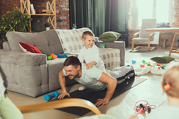 Image showing Young man exercising fitness, aerobic, yoga at home, sporty lifestyle. Getting active while his child playing on the background, home gym.