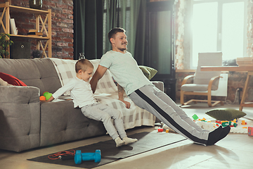 Image showing Young man exercising fitness, aerobic, yoga at home, sporty lifestyle. Getting active while his child playing on the background, home gym.