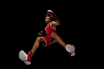 Image showing Young african-american boxer in action, motion isolated on black background, look from the bottom. Concept of sport, movement, energy and dynamic.