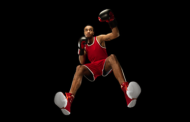 Image showing Young african-american boxer in action, motion isolated on black background, look from the bottom. Concept of sport, movement, energy and dynamic.