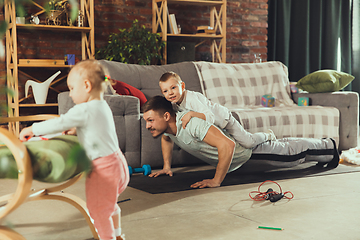 Image showing Young man exercising fitness, aerobic, yoga at home, sporty lifestyle. Getting active while his child playing on the background, home gym.