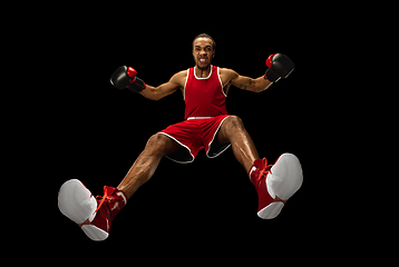 Image showing Young african-american boxer in action, motion isolated on black background, look from the bottom. Concept of sport, movement, energy and dynamic.