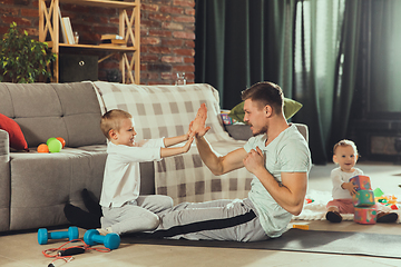 Image showing Young man exercising fitness, aerobic, yoga at home, sporty lifestyle. Getting active while his child playing on the background, home gym.