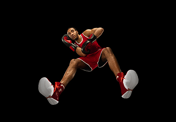 Image showing Young african-american boxer in action, motion isolated on black background, look from the bottom. Concept of sport, movement, energy and dynamic.