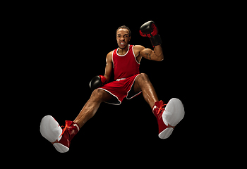 Image showing Young african-american boxer in action, motion isolated on black background, look from the bottom. Concept of sport, movement, energy and dynamic.