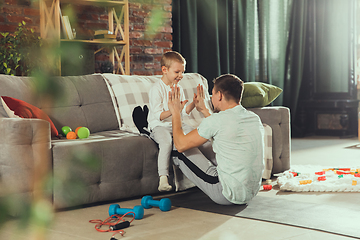 Image showing Young man exercising fitness, aerobic, yoga at home, sporty lifestyle. Getting active while his child playing on the background, home gym.