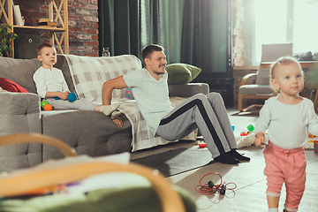 Image showing Young man exercising fitness, aerobic, yoga at home, sporty lifestyle. Getting active while his child playing on the background, home gym.