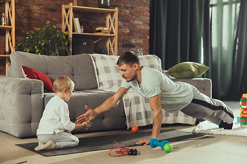 Image showing Young man exercising fitness, aerobic, yoga at home, sporty lifestyle. Getting active while his child playing on the background, home gym.