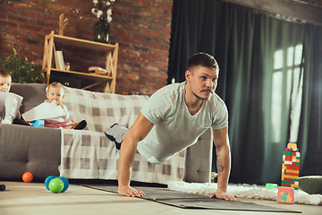 Image showing Young man exercising fitness, aerobic, yoga at home, sporty lifestyle. Getting active while his child playing on the background, home gym.