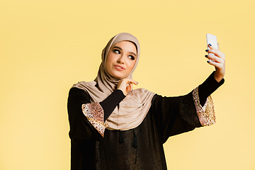 Image showing Beautiful arab woman posing in stylish hijab isolated on yellow studio background. Fashion, beauty, style concept