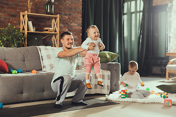 Image showing Young man exercising fitness, aerobic, yoga at home, sporty lifestyle. Getting active while his child playing on the background, home gym.