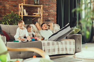 Image showing Young man exercising fitness, aerobic, yoga at home, sporty lifestyle. Getting active while his child playing on the background, home gym.