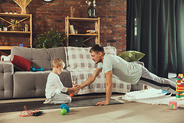 Image showing Young man exercising fitness, aerobic, yoga at home, sporty lifestyle. Getting active while his child playing on the background, home gym.