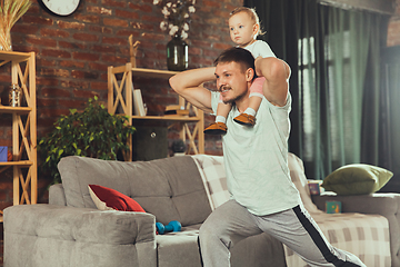 Image showing Young man exercising fitness, aerobic, yoga at home, sporty lifestyle. Getting active while his child playing on the background, home gym.