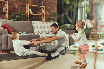 Image showing Young man exercising fitness, aerobic, yoga at home, sporty lifestyle. Getting active while his child playing on the background, home gym.