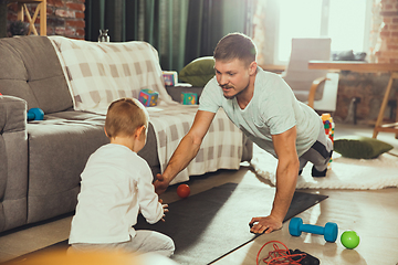 Image showing Young man exercising fitness, aerobic, yoga at home, sporty lifestyle. Getting active while his child playing on the background, home gym.