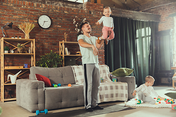 Image showing Young man exercising fitness, aerobic, yoga at home, sporty lifestyle. Getting active while his child playing on the background, home gym.