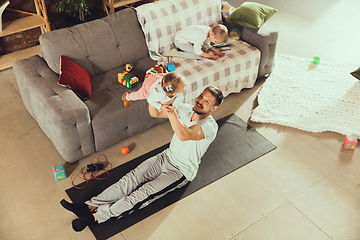 Image showing Young man exercising fitness, aerobic, yoga at home, sporty lifestyle. Getting active while his child playing on the background, home gym.