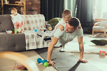 Image showing Young man exercising fitness, aerobic, yoga at home, sporty lifestyle. Getting active while his child playing on the background, home gym.