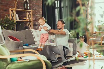 Image showing Young man exercising fitness, aerobic, yoga at home, sporty lifestyle. Getting active while his child playing on the background, home gym.