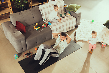 Image showing Young man exercising fitness, aerobic, yoga at home, sporty lifestyle. Getting active while his child playing on the background, home gym.