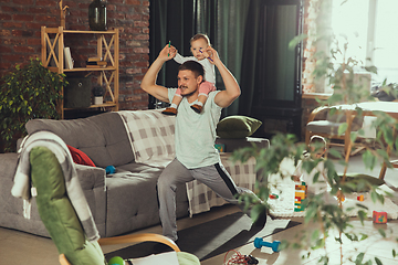 Image showing Young man exercising fitness, aerobic, yoga at home, sporty lifestyle. Getting active while his child playing on the background, home gym.