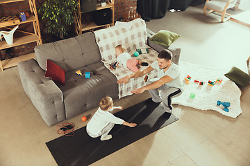 Image showing Young man exercising fitness, aerobic, yoga at home, sporty lifestyle. Getting active while his child playing on the background, home gym.