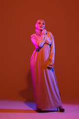 Image showing Beautiful arab woman posing in stylish hijab isolated on brown studio background in neon light. Fashion, beauty, style concept