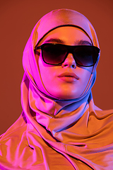 Image showing Beautiful arab woman posing in stylish hijab isolated on brown studio background in neon light. Fashion, beauty, style concept