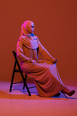 Image showing Beautiful arab woman posing in stylish hijab isolated on brown studio background in neon light. Fashion, beauty, style concept