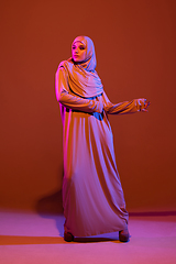 Image showing Beautiful arab woman posing in stylish hijab isolated on brown studio background in neon light. Fashion, beauty, style concept